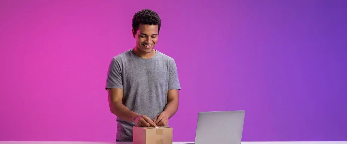 Empreendedor embalando um pedido ao lado do laptop